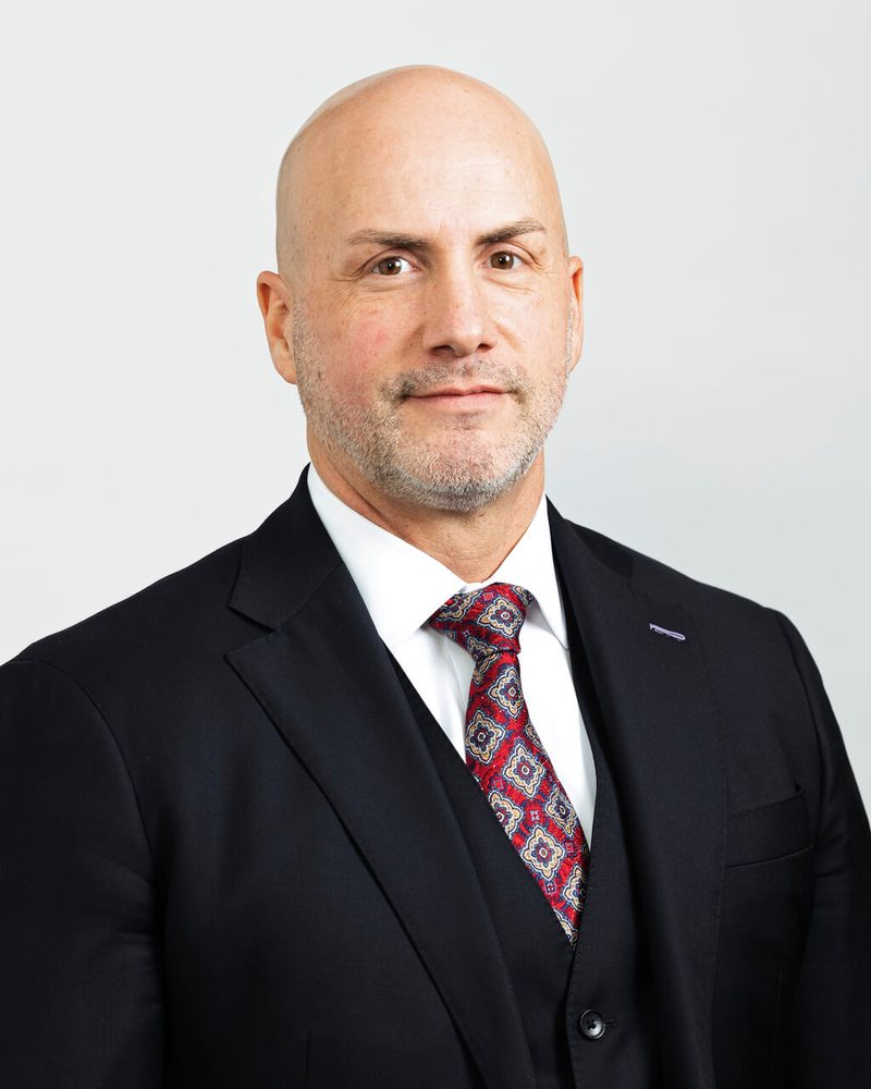 Portrait of Matthew Merrill in a dark suit and patterned red tie